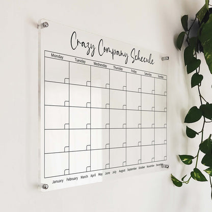Angled close-up of the personalized company schedule acrylic calendar mounted near a hanging plant