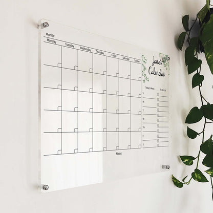 Angled close-up of the floral 'Jane's Calendar' acrylic monthly planner mounted beside a hanging plant