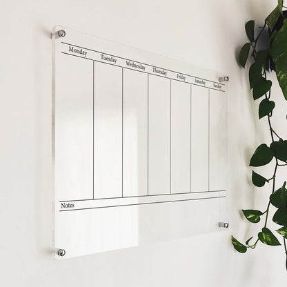 Angled close-up of the minimalist acrylic weekly planner mounted near a hanging plant