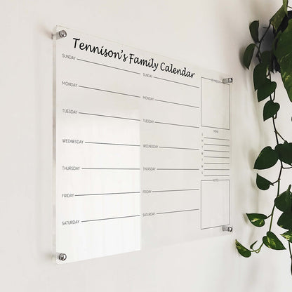 Angled close-up of 'Tennison's Family Calendar' acrylic command center mounted beside a hanging plant