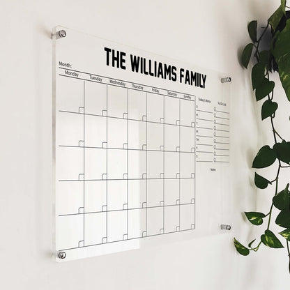 Angled close-up of the bold-title 'The Williams Family' acrylic calendar mounted beside a hanging plant