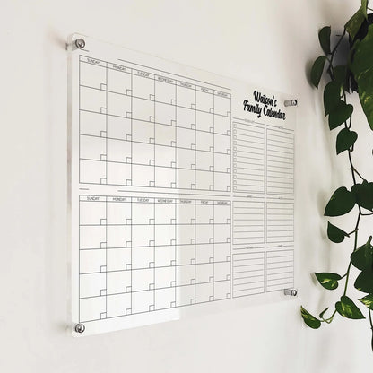 Angled close-up of the 'Watson's Family Calendar' acrylic planner mounted beside a hanging plant