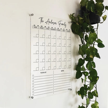 Angled close-up of 'The Anderson Family' vertical acrylic calendar mounted beside a hanging plant