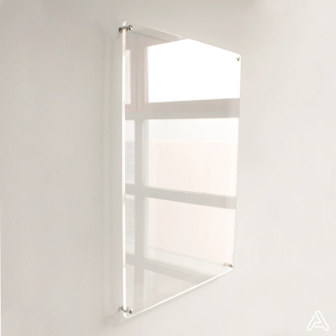 Blank clear acrylic dry-erase board mounted on a white wall with silver standoff hardware, angled view